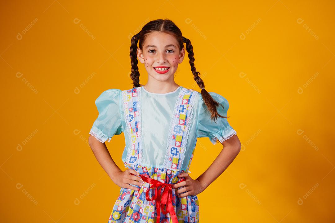 Criança com roupas típicas da famosa festa brasileira chamada Festa Junina em comemoração ao São João. Linda garota em fundo amarelo.