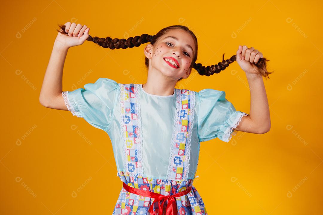 Criança com roupas típicas da famosa festa brasileira chamada Festa Junina em comemoração ao São João. Linda garota em fundo amarelo.