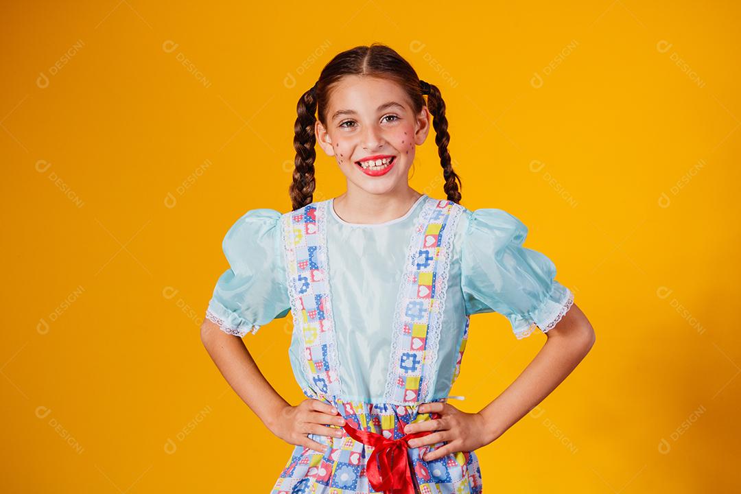 Criança com roupas típicas da famosa festa brasileira chamada Festa Junina em comemoração ao São João. Linda garota em fundo amarelo.
