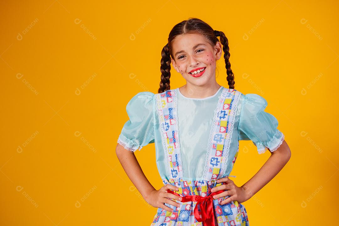 Criança com roupas típicas da famosa festa brasileira chamada Festa Junina em comemoração ao São João. Linda garota em fundo amarelo.