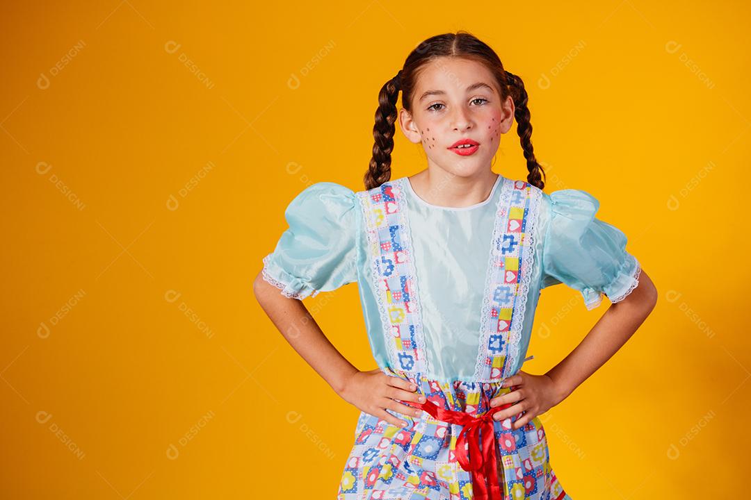 Criança com roupas típicas da famosa festa brasileira chamada Festa Junina em comemoração ao São João. Linda garota em fundo amarelo.