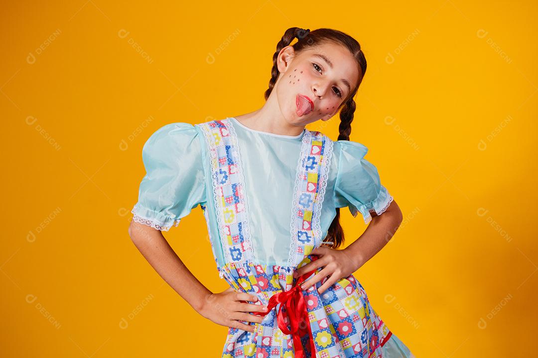 Criança com roupas típicas da famosa festa brasileira chamada Festa Junina em comemoração ao São João. Linda garota em fundo amarelo.