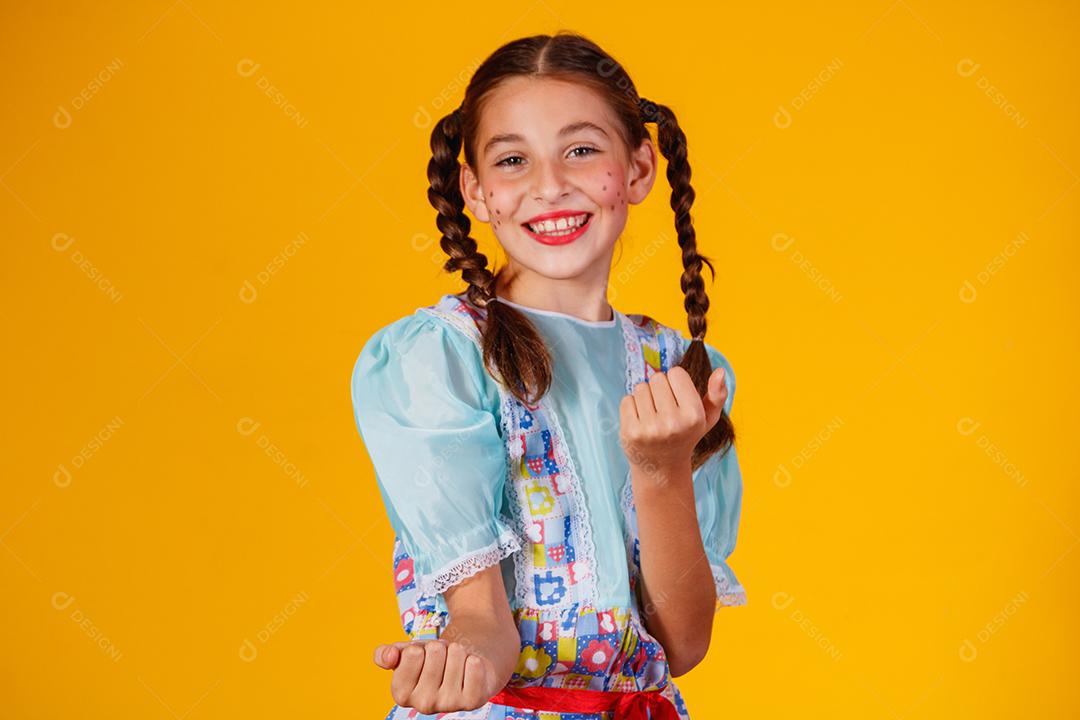 Criança com roupas típicas da famosa festa brasileira chamada Festa Junina em comemoração ao São João. Linda garota em fundo amarelo.