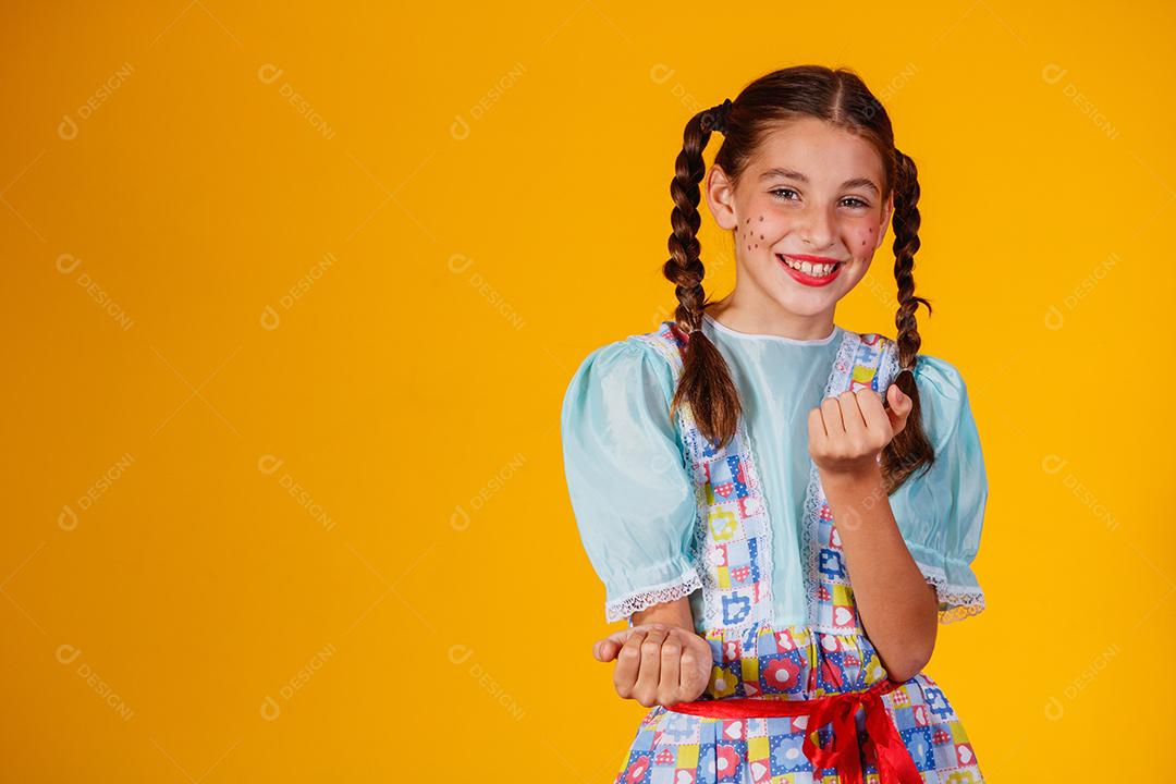 Criança com roupas típicas da famosa festa brasileira chamada Festa Junina em comemoração ao São João. Linda garota em fundo amarelo.