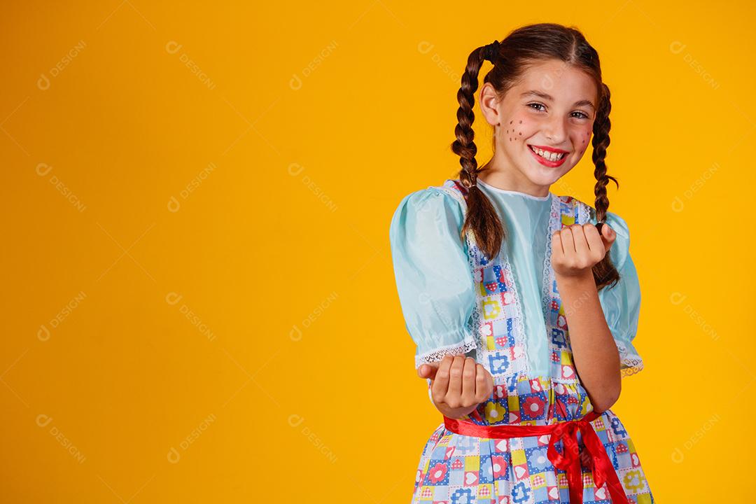 Criança com roupas típicas da famosa festa brasileira chamada Festa Junina em comemoração ao São João. Linda garota em fundo amarelo.