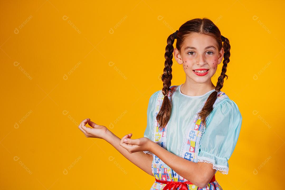 Criança com roupas típicas da famosa festa brasileira chamada Festa Junina em comemoração ao São João. Linda garota em fundo amarelo.