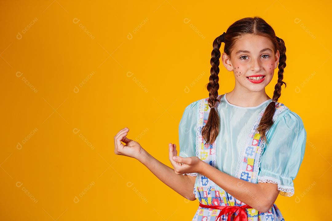 Criança com roupas típicas da famosa festa brasileira chamada Festa Junina em comemoração ao São João. Linda garota em fundo amarelo.