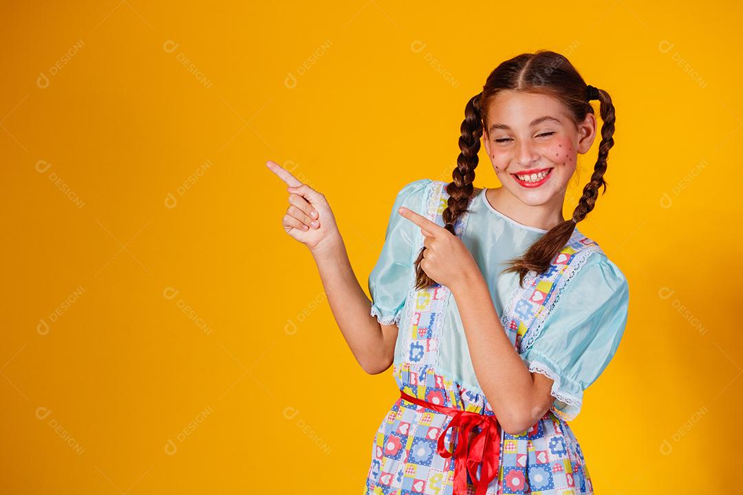 Criança com roupas típicas da famosa festa brasileira chamada Festa Junina em comemoração ao São João. Linda garota em fundo amarelo.