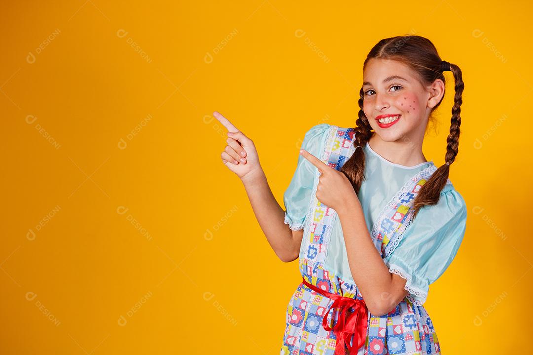 Criança com roupas típicas da famosa festa brasileira chamada Festa Junina em comemoração ao São João. Linda garota em fundo amarelo.