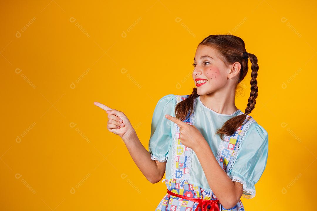 Criança com roupas típicas da famosa festa brasileira chamada Festa Junina em comemoração ao São João. Linda garota em fundo amarelo.