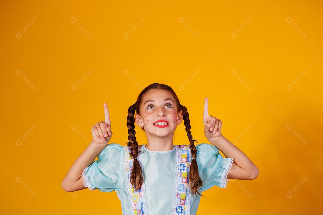 Criança com roupas típicas da famosa festa brasileira chamada Festa Junina em comemoração ao São João. Linda garota em fundo amarelo.
