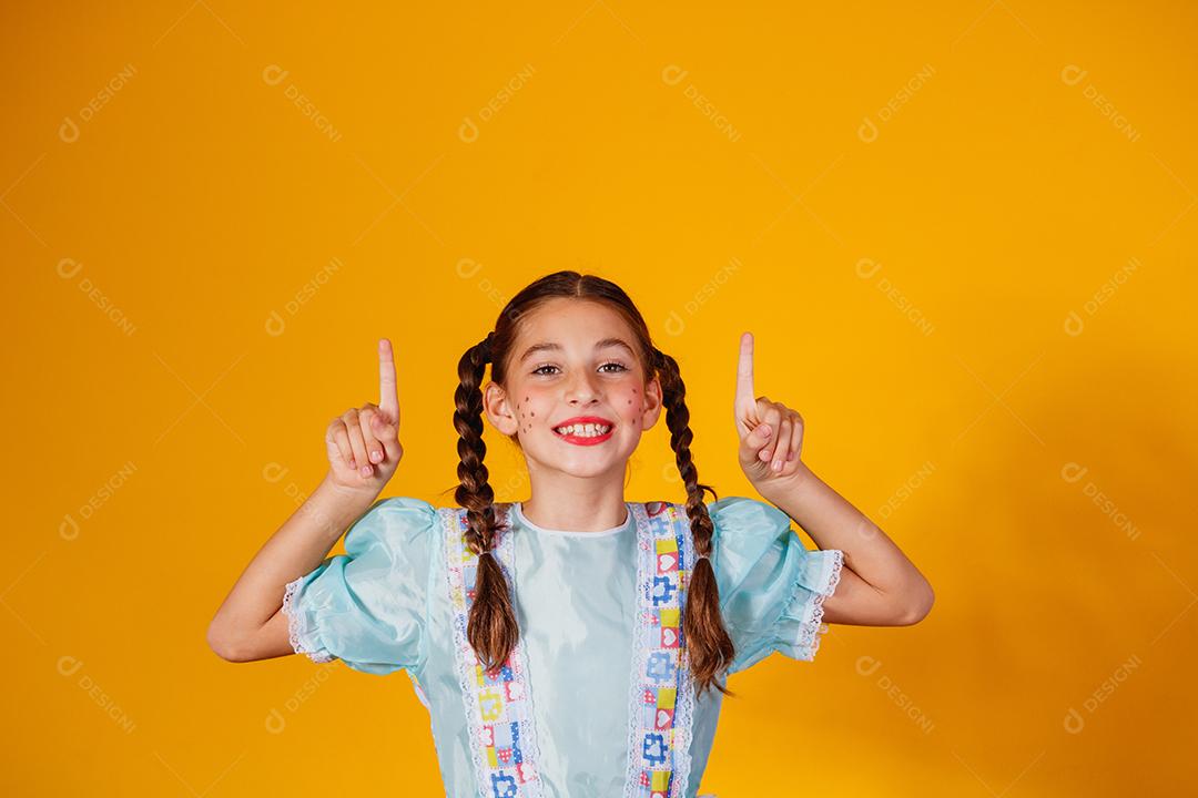 Criança com roupas típicas da famosa festa brasileira chamada Festa Junina em comemoração ao São João. Linda garota em fundo amarelo.