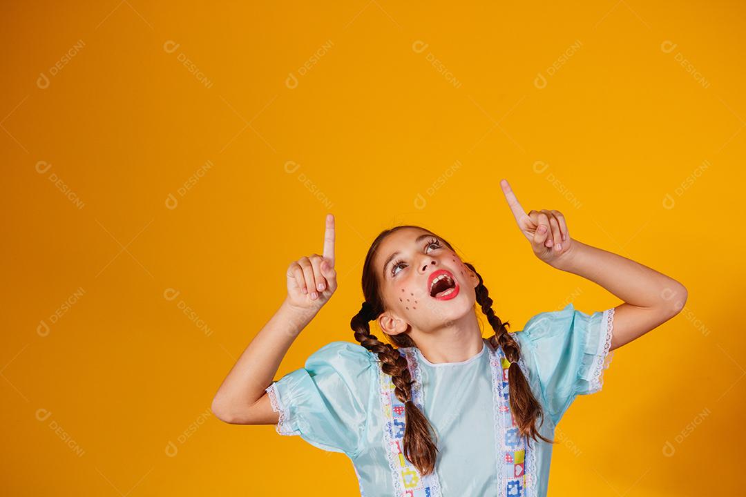 Criança com roupas típicas da famosa festa brasileira chamada Festa Junina em comemoração ao São João. Linda garota em fundo amarelo.