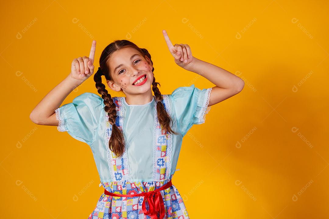 Criança com roupas típicas da famosa festa brasileira chamada Festa Junina em comemoração ao São João. Linda garota em fundo amarelo.