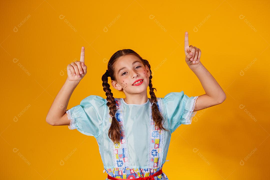 Criança com roupas típicas da famosa festa brasileira chamada Festa Junina em comemoração ao São João. Linda garota em fundo amarelo.