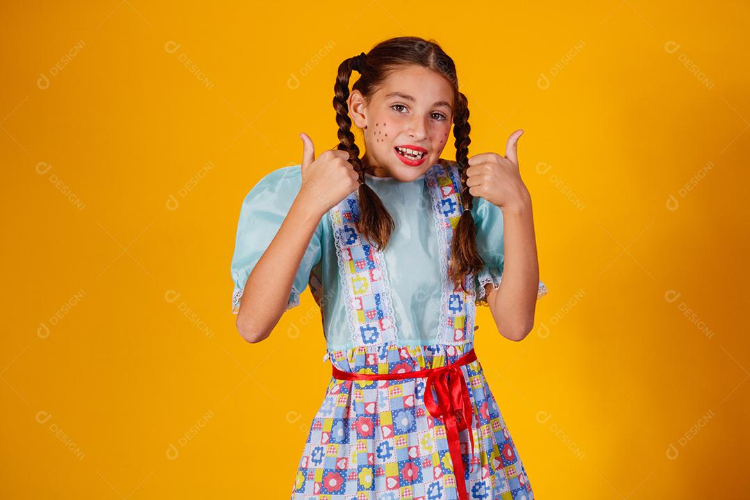 Criança com roupas típicas da famosa festa brasileira chamada Festa Junina em comemoração ao São João. Linda garota em fundo amarelo.