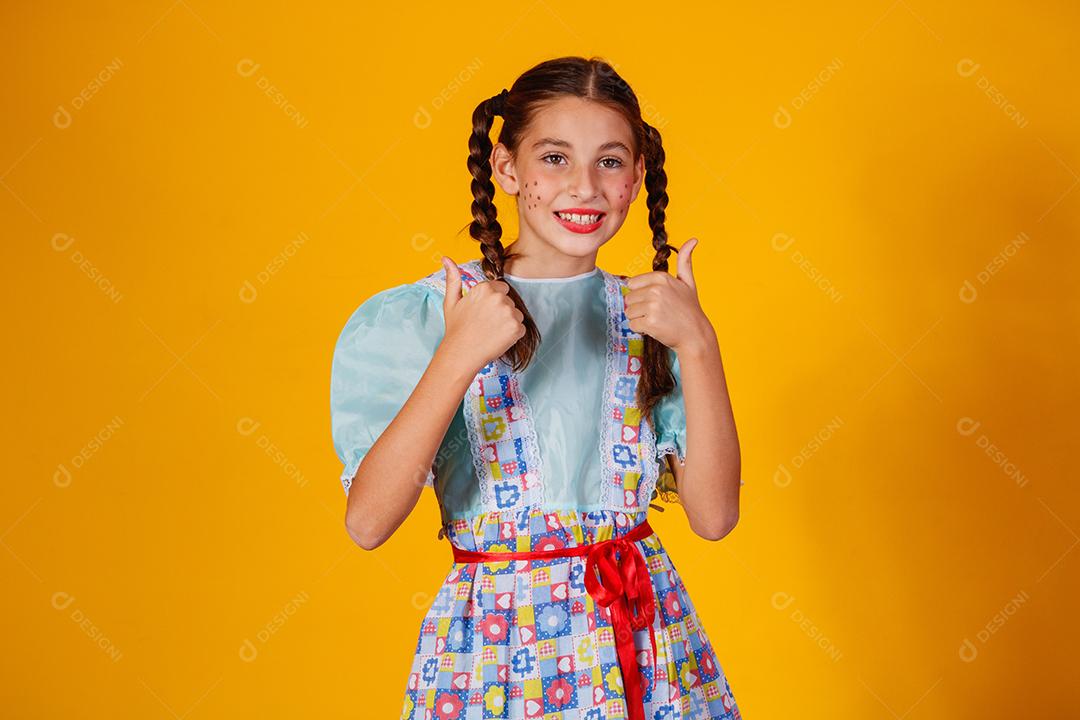 Criança com roupas típicas da famosa festa brasileira chamada Festa Junina em comemoração ao São João. Linda garota em fundo amarelo.