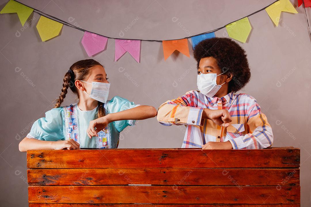 Crianças vestindo roupas típicas para a Festa Junina e máscara de proteção para prevenção do COVID-19.