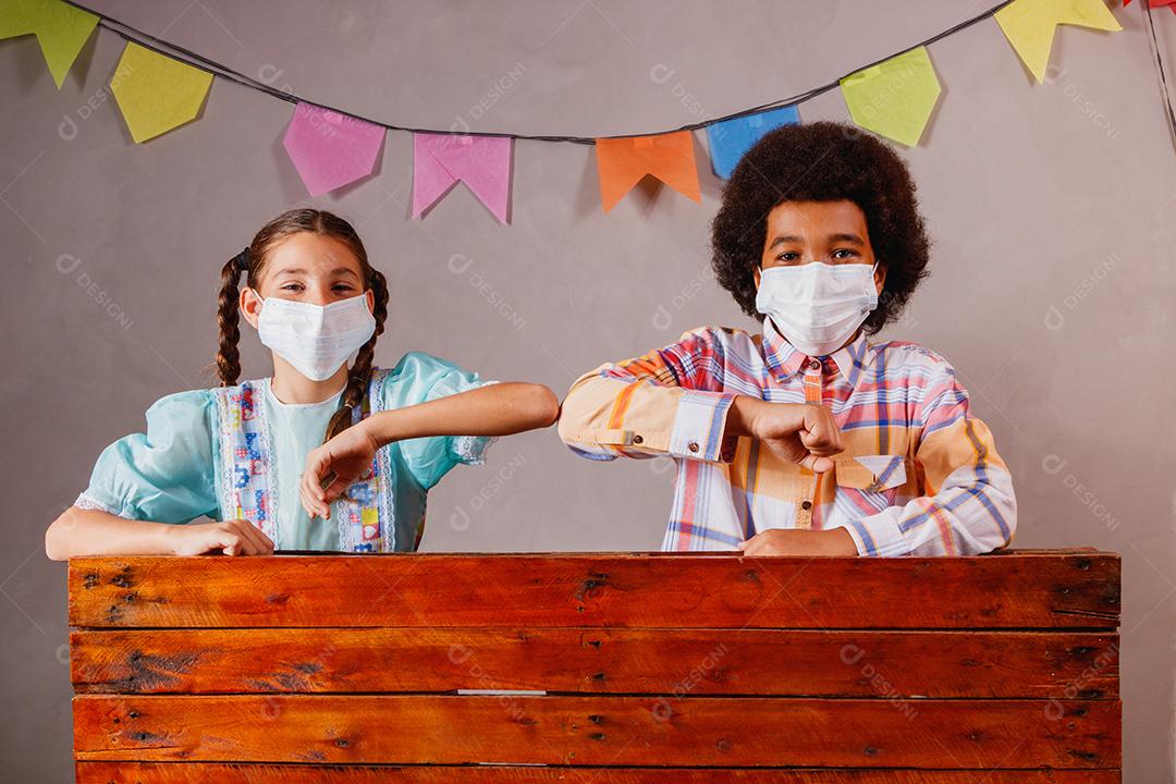 Crianças vestindo roupas típicas para a Festa Junina e máscara de proteção para prevenção do COVID-19.