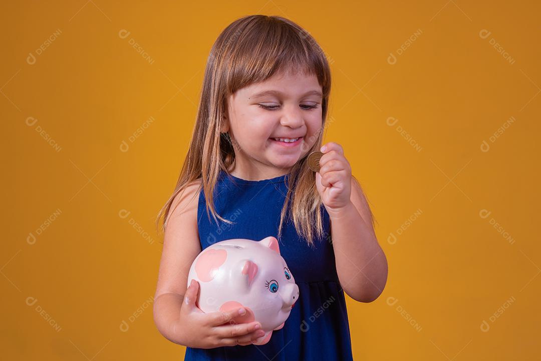 Criança pequena com cofrinho em fundo amarelo