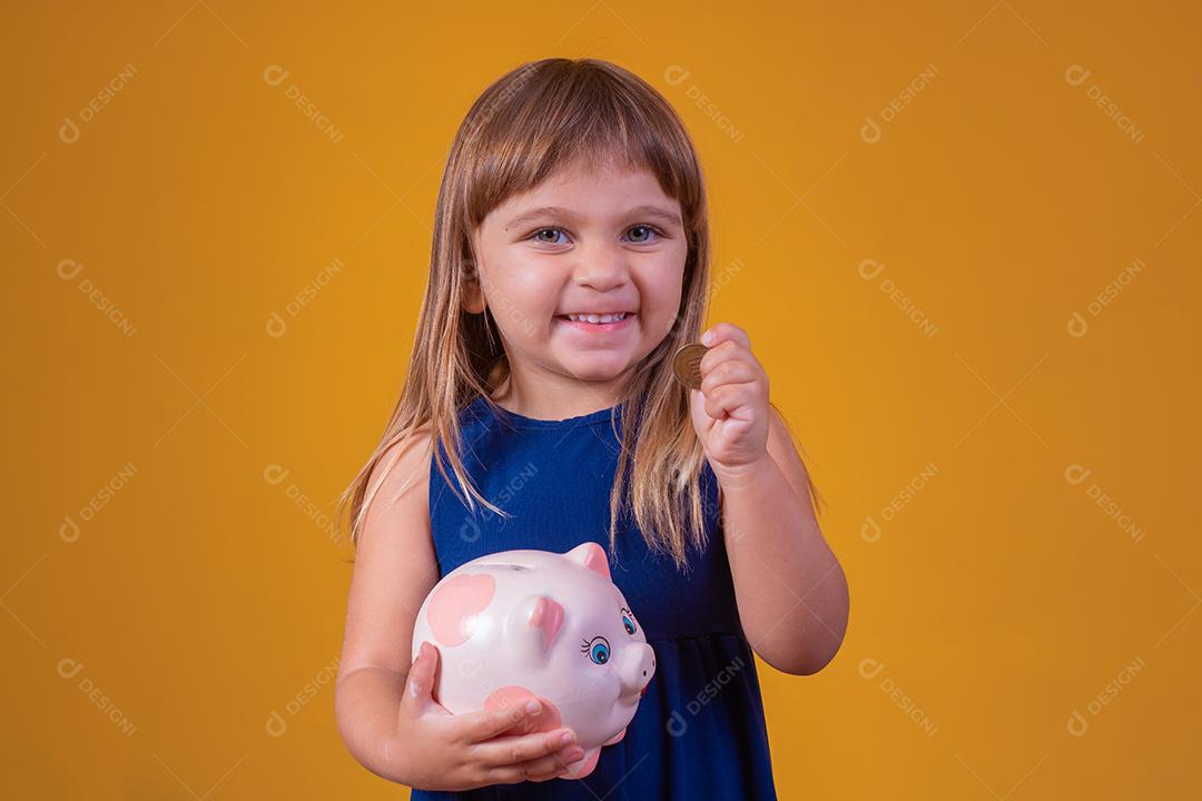 Small child with piggy bank on yellow background