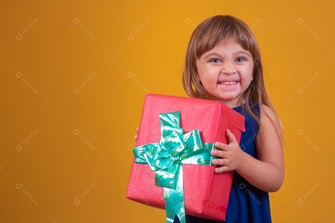 menina feliz segurando um presente em fundo amarelo.