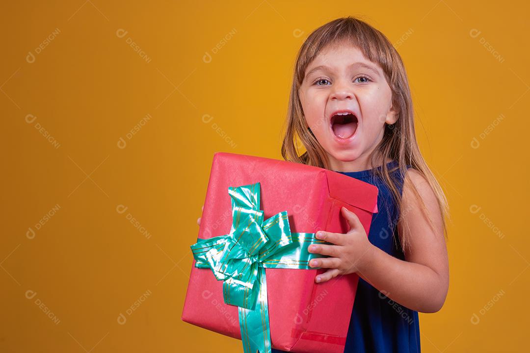 menina feliz segurando um presente em fundo amarelo.