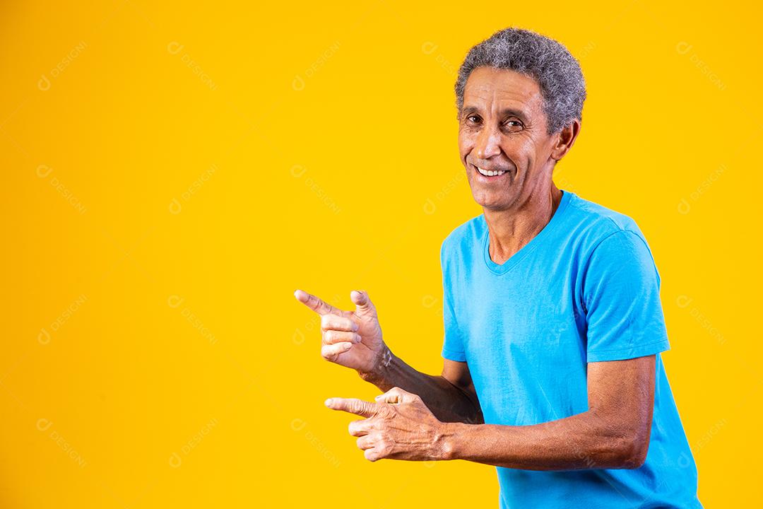 Homem idoso apontando para o lado em fundo amarelo