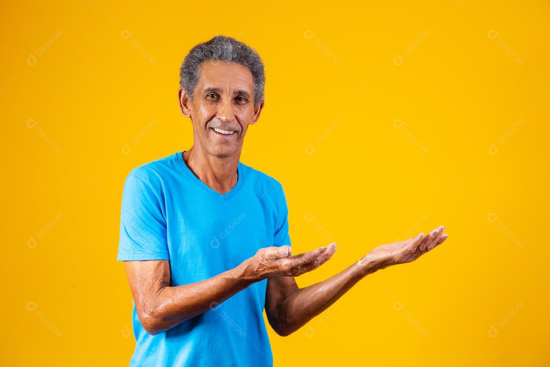 Homem idoso apontando para o lado em fundo amarelo
