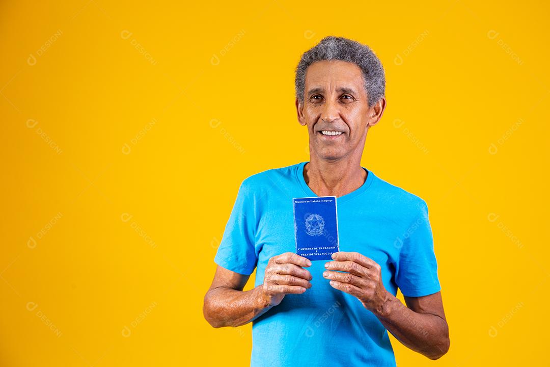 Homem idoso segurando carteira de trabalho em fundo amarelo
