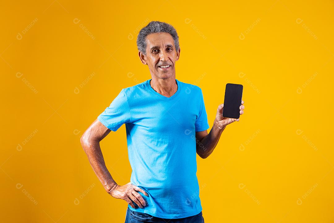 Homem idoso segurando celular em fundo amarelo