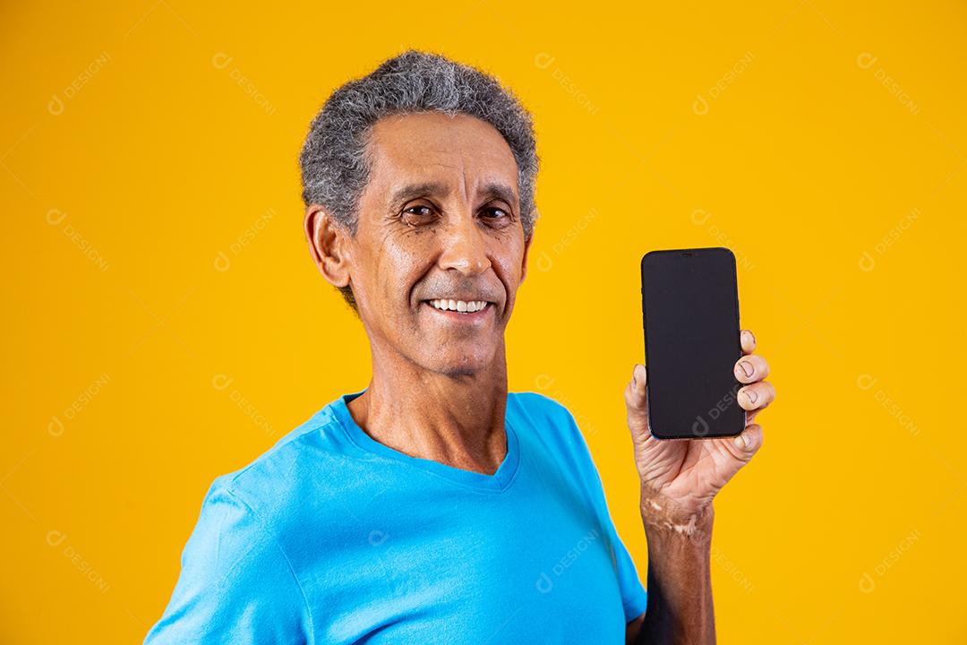 Homem idoso segurando celular em fundo amarelo
