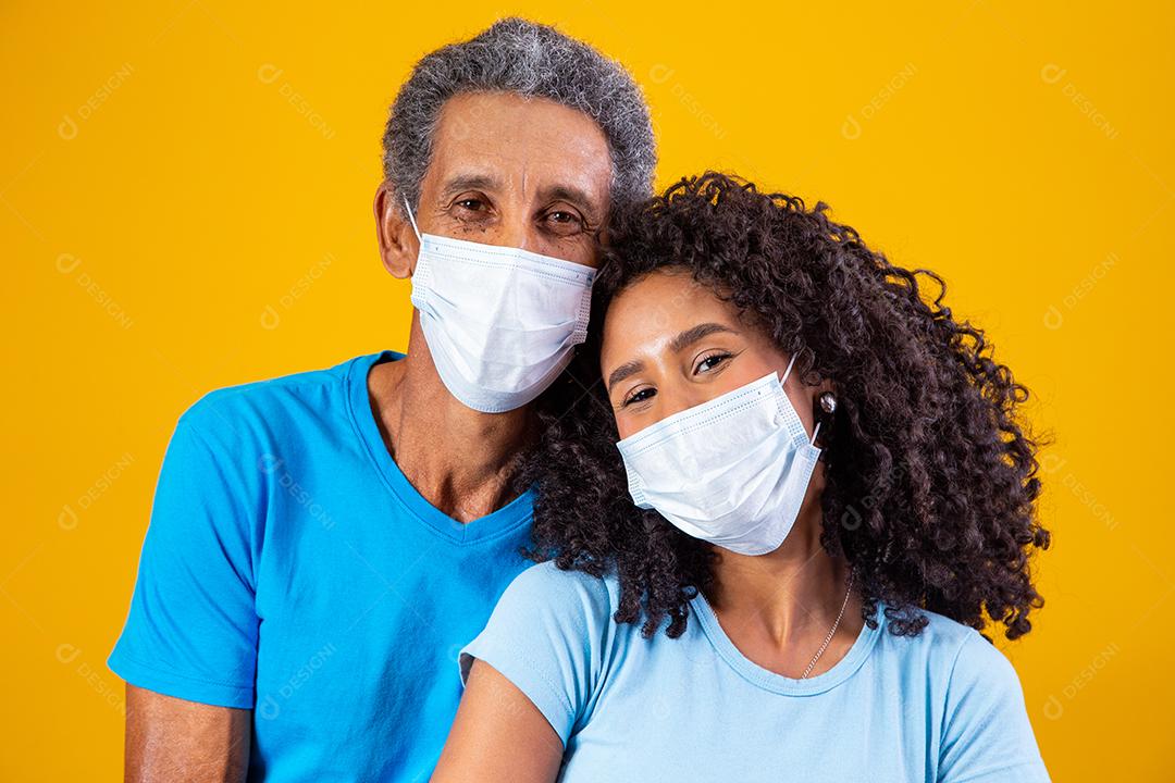 Pai abraçado com filha usando mascara em fundo amarelo