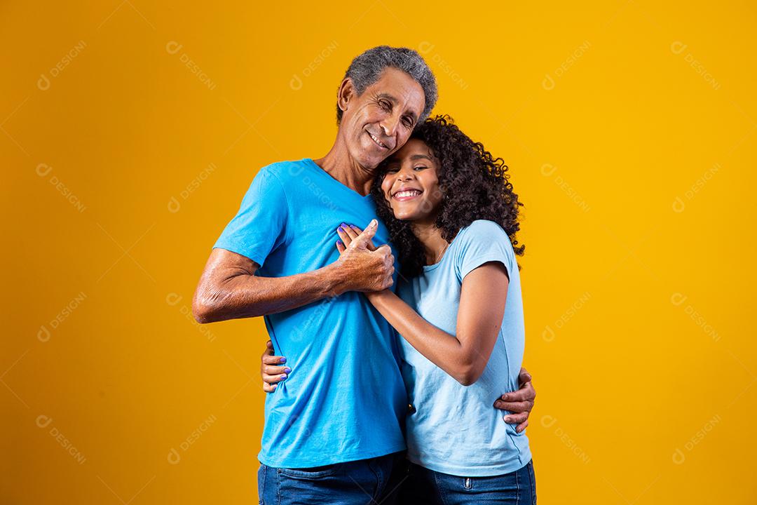 Pai abraçado com filha ambos usando camisa azul em fundo amarelo