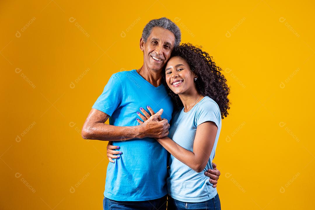 Pai abraçado com filha ambos usando camisa azul em fundo amarelo