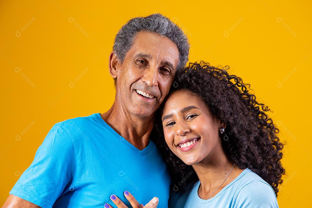 Pai abraçado com filha ambos usando camisa azul em fundo amarelo