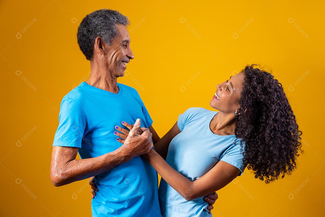 Pai abraçado com filha ambos usando camisa azul em fundo amarelo