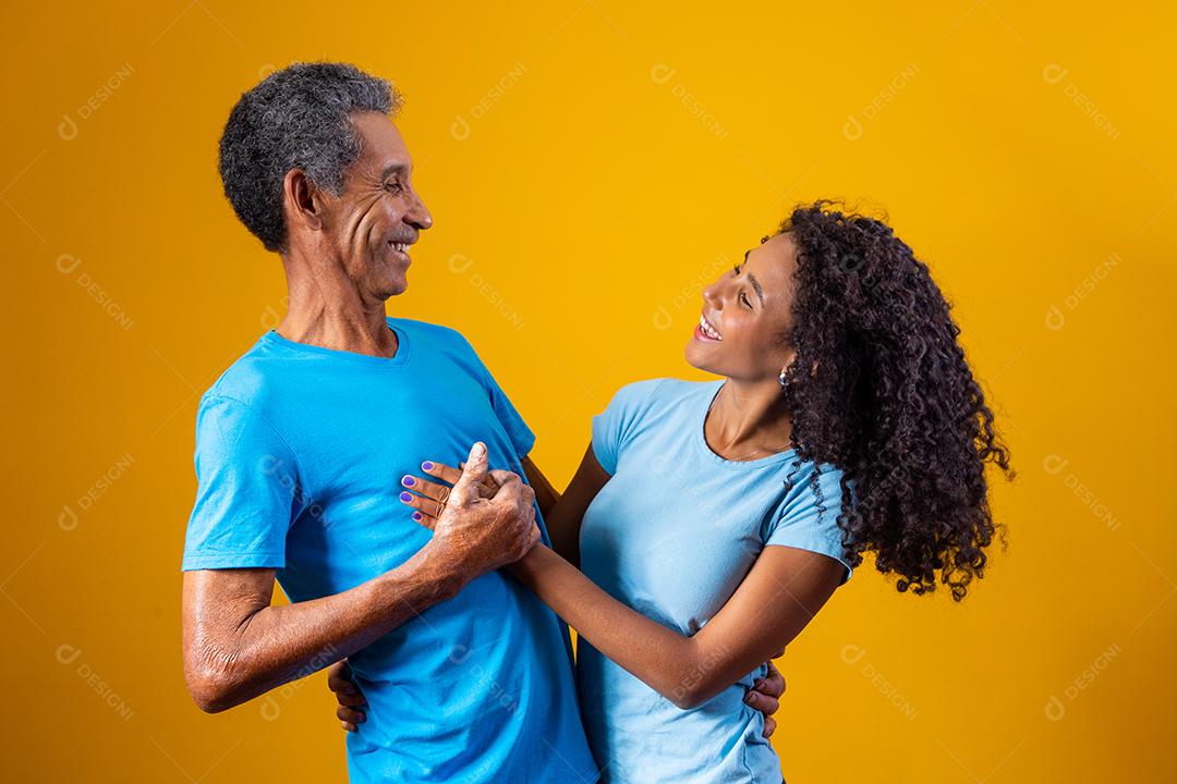 Pai abraçado com filha ambos usando camisa azul em fundo amarelo