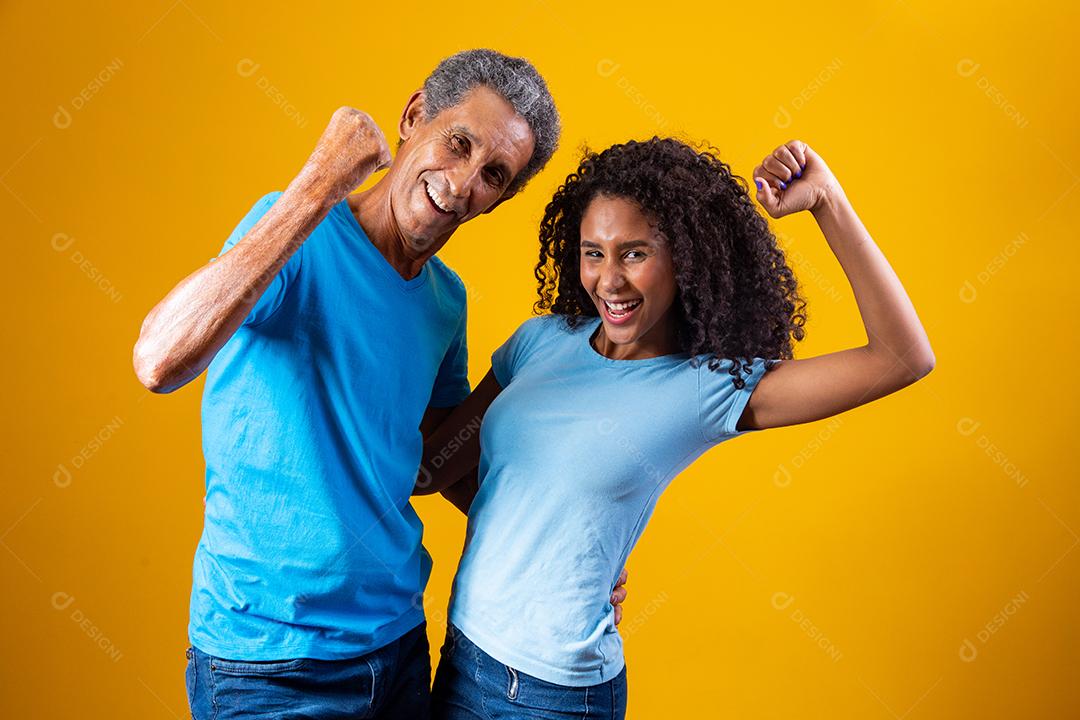 Pai e filha abraçados fazendo com mãos para cima  em fundo amarelo