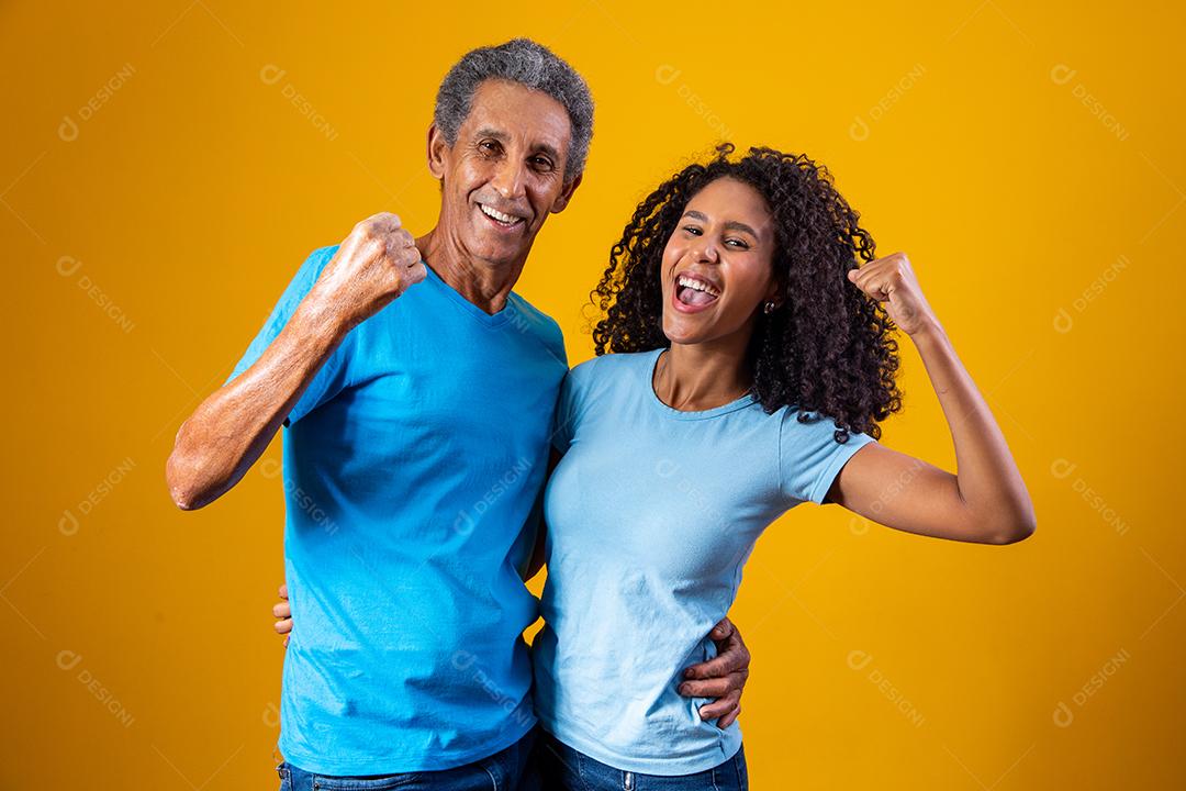 Pai e filha abraçados com camisetas azuis em fundo amarelo