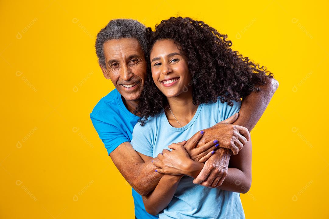 Pai abraçado com filha ambos usando camisa azul em fundo amarelo