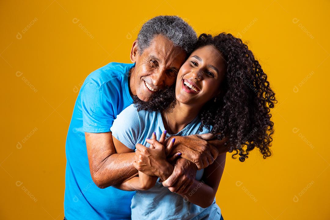 Pai e filha abraçados com camisetas azuis em fundo amarelo