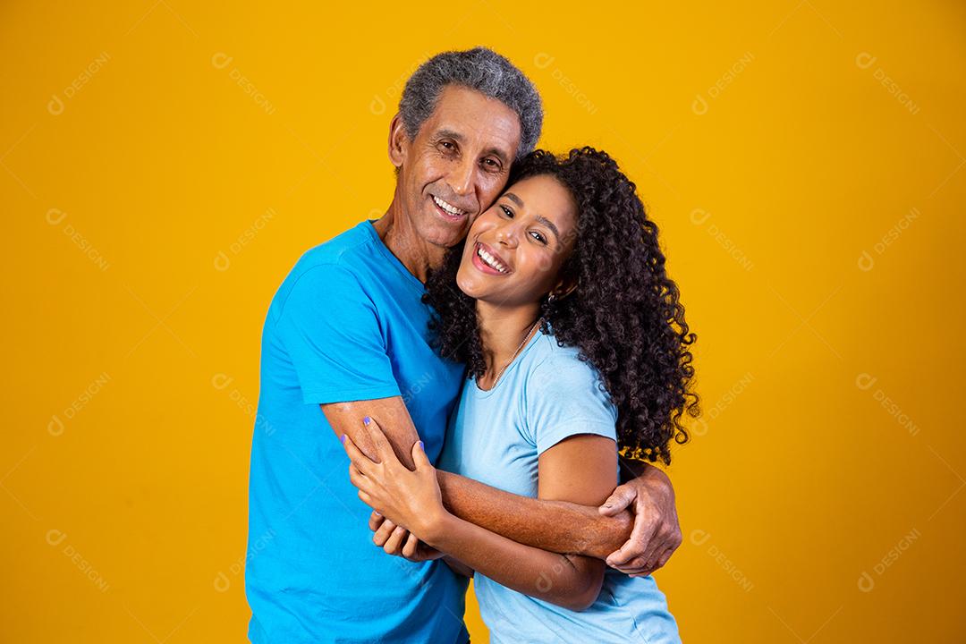 Pai e filha abraçados com camisetas azuis em fundo amarelo
