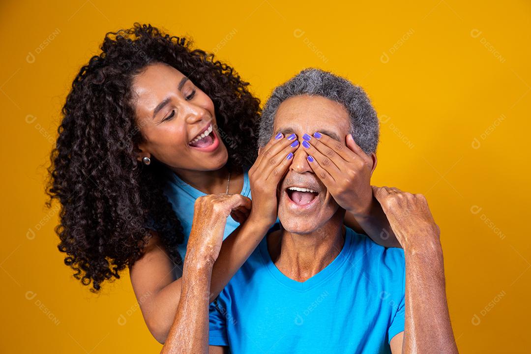 Pai e filha abraçados com camisetas azuis em fundo amarelo