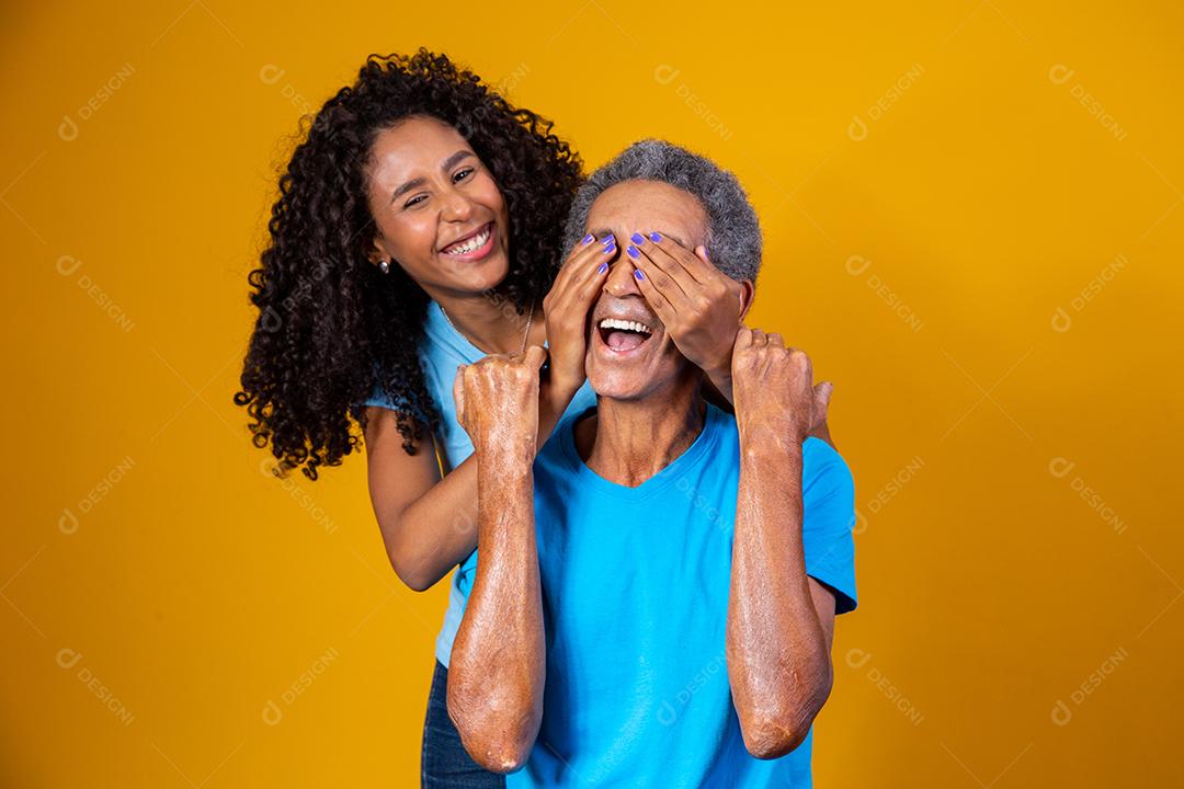 Pai e filha abraçados com camisetas azuis em fundo amarelo