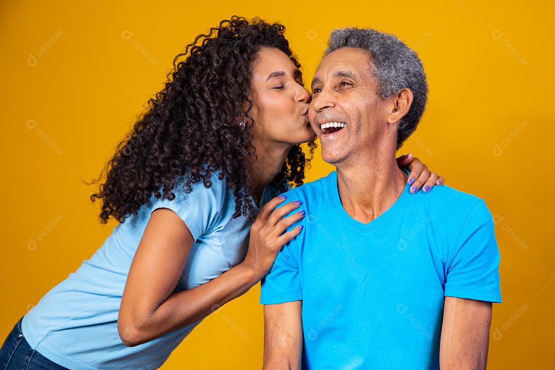 Pai e filha abraçados com camisetas azuis em fundo amarelo
