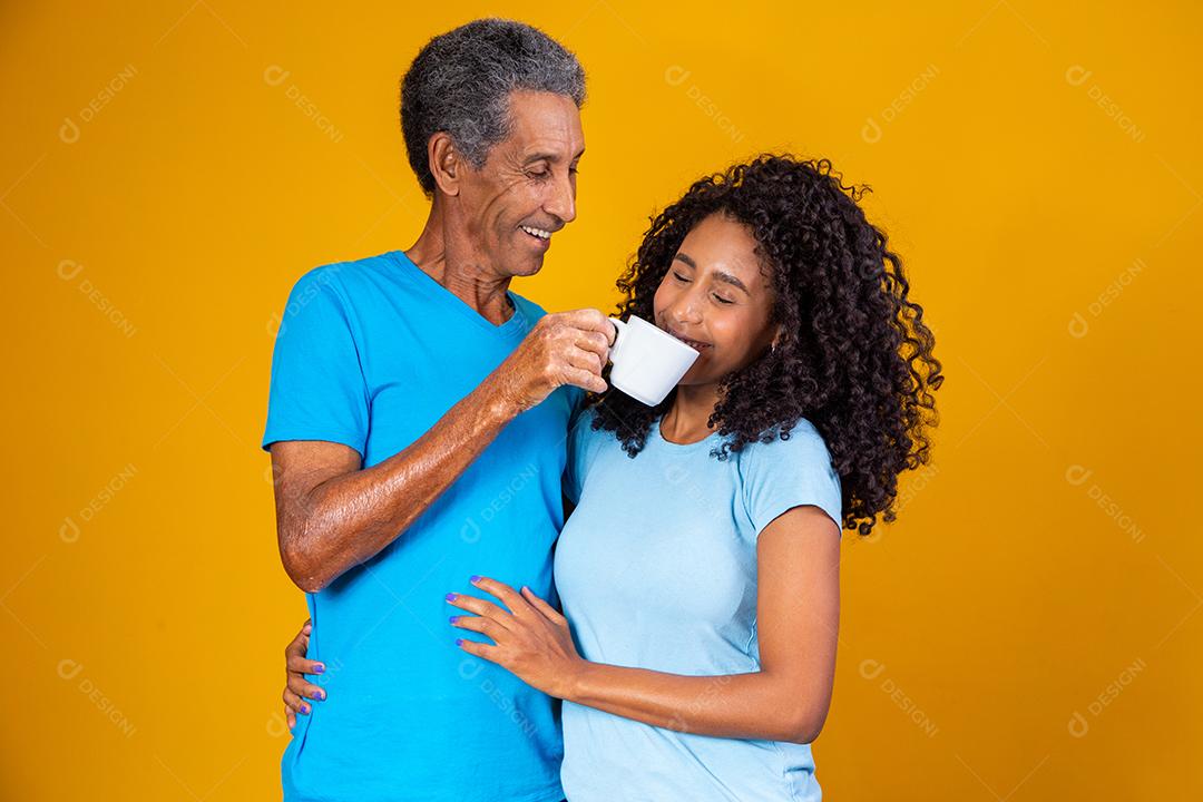 Pai dando bebida em xicara para filha em fundo amarelo