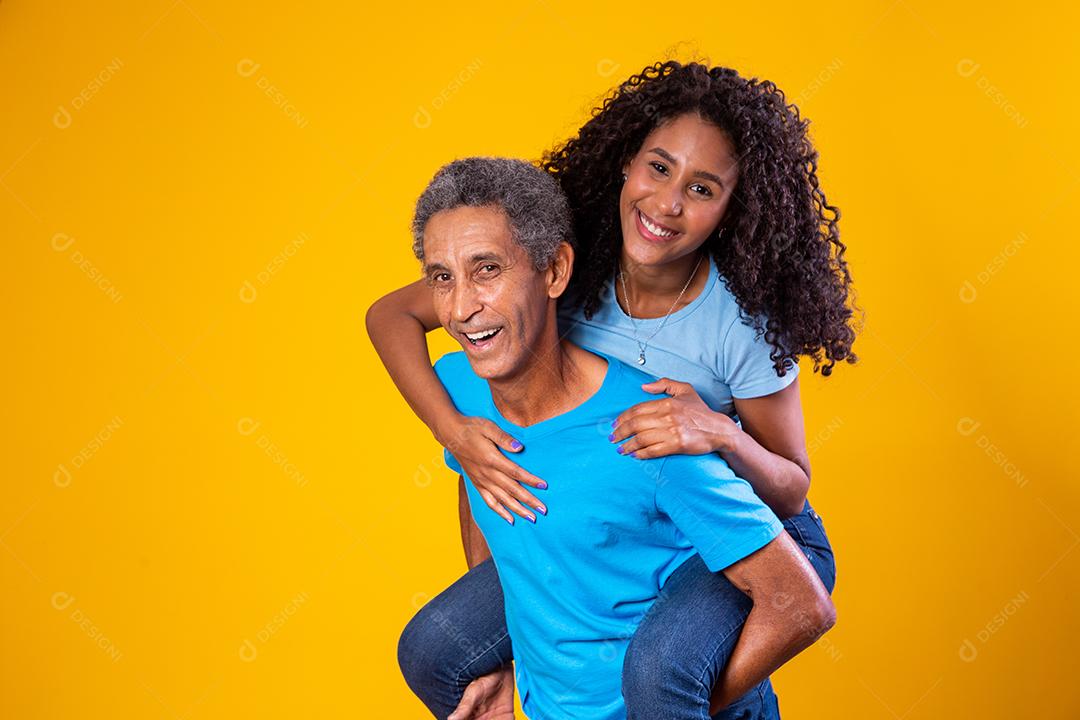 Filha montada em costas do pai com camisas azuis em fundo amarelo