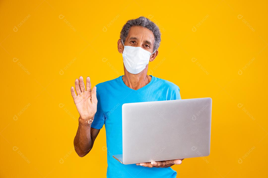 Homem em vídeo chamada segurando notebook em fundo amarelo