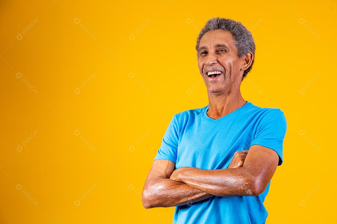 Retrato de homem idoso afro com os braços cruzados, sorrindo para a câmera.